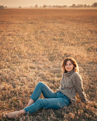 Portrait of a beautiful young model in warm clothes enjoy day, on background field in  sunny autumn day . Autumn warm photo. Woman smiling and look away, joyful cheerful mood.