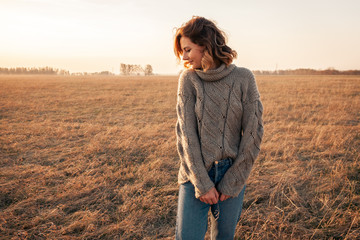 Outdoor atmospheric lifestyle photo of young beautiful  darkhaired woman  brown knit sweater made of natural wool and jeans in sunny autumn day, on background field