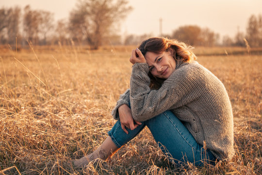 Portrait of a beautiful young model in warm clothes enjoy day, on background field in  sunny autumn day . Autumn warm photo. Woman smiling and look away, joyful cheerful mood.