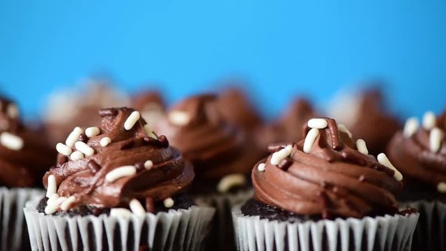 Chocolate iced cupcakes rotating against a blue background