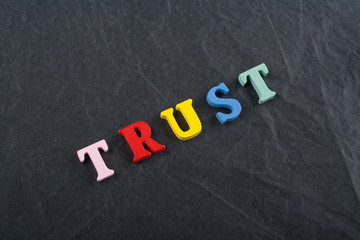 TRUST word on black board background composed from colorful abc alphabet block wooden letters, copy space for ad text. Learning english concept.