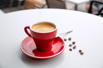 Red cappuccino coffee cup mug on a white cafe table interior with menu