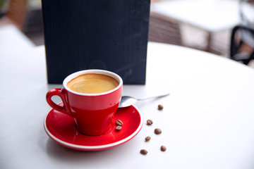 Red cappuccino coffee cup mug on a white cafe table interior with menu