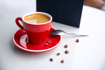Red cappuccino coffee cup mug on a white cafe table interior with menu