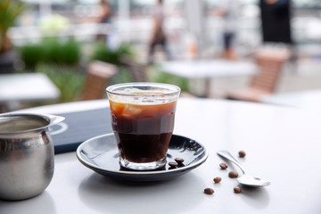 Freshly poured hot black coffee in glass at cafe table