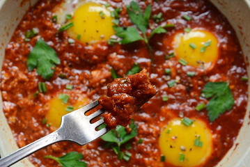 Shakshuka , middle eastern traditional homemade breakfast- fried eggs, onion, bell pepper, tomatoes and parsley in a pan on a wooden background served with hummus