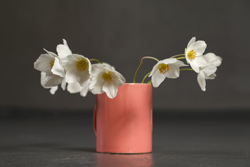Beautiful white wildflowers in a pink glass on a gray background.
