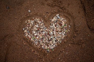 A heart made out of sand and sea glass at the beach.
