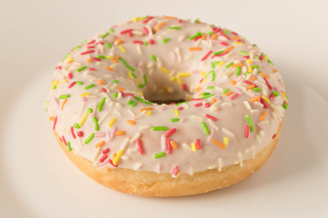 Fresh glazed donut with colorful sprinkles on a white plate.