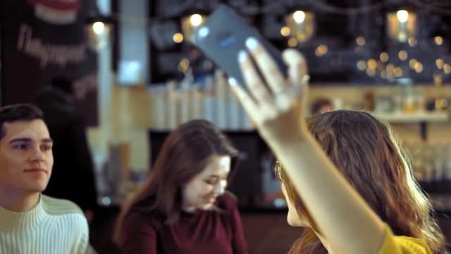 Meeting friends at a coffee shop. A young attractive girl in glasses does the picture on the smartphone.