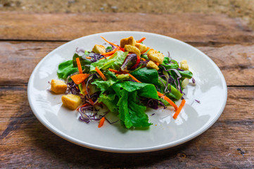 Salad of fresh vegetables in a white dish placed on an old wooden table.