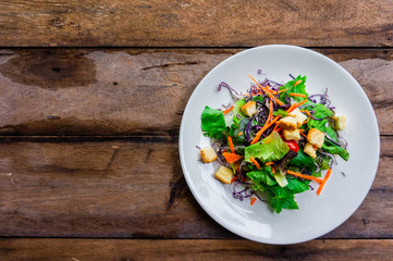 Salad of fresh vegetables in a white dish placed on an old wooden table.top view.