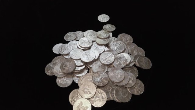 American Silver Eagle silver coins falling into a pile in slow motion.