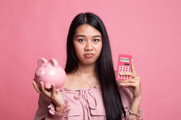 Unhappy Asian woman with calculator and piggy bank.