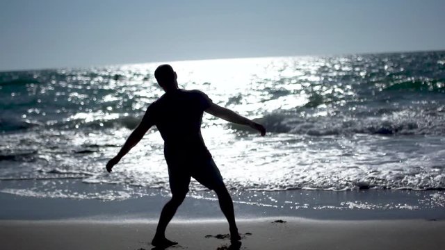 Man practicing yoga and tai chi at sunset at the beach. Slow motion Silhouette