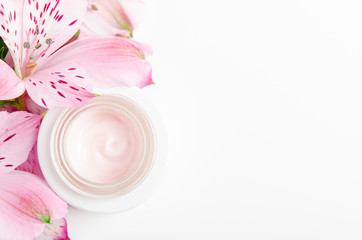 Face cream in white jar on a white background with pink flowers. Concept natural cosmetics, organic beauty, flower arrangement. Copy space, top view, flat lay.