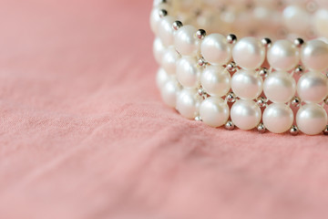 Beautiful white pearl bracelet on a coral textile background close up