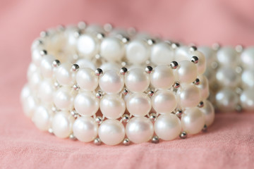 Beautiful white pearl necklace on a coral color textile background close up