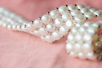 Beautiful white pearl necklace on a coral color textile background close up