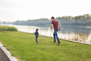 Parenthood and children concept - Father playing with a little son, trying to catch him