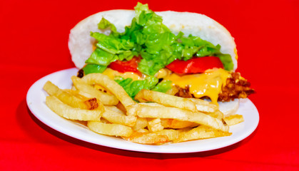 Sandwiches fried chicken, tomatoes, lettuce leaves and French fries with red background.