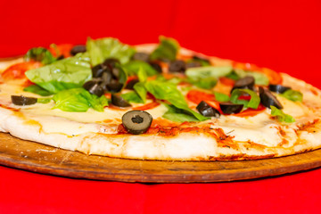 Pizza, black olives, green leaf decoration and peppers. Red background.
