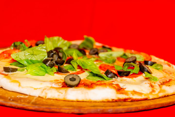 Pizza, black olives, green leaf decoration and peppers. Red background.