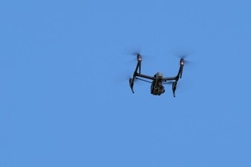 Drone with a video camera flies in the blue cloudless sky. Videofilming and videosurveillance from above. Copy space.