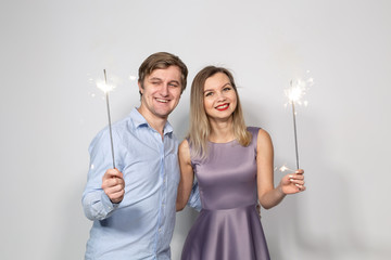 Party, celebration, event and holidays concept - man dressed in blue shirt and woman dressed in purple dress hold a firework stick