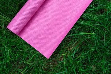 Pink yoga mat on fresh green grass. Equipment for yoga. Concept healthy lifestyle, sport and wellness. Copy space