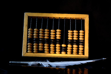 Wooden abacus and quill pen on a black background. Concept - retro accounting