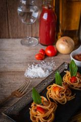 Spaghetti in Tomato sauce fit the pieces on the black plate placed on the wood table there are fork, tomato, sauce, oil, onion, salt and raw spaghetti placed around.