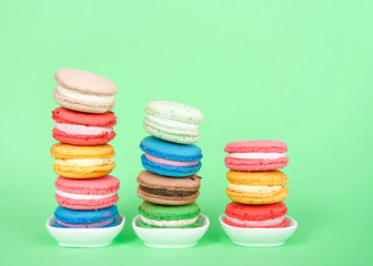 Macaron cookies in tiny white dishes stacked in graduated rows, colorful traditional french pastry on a mint green background.