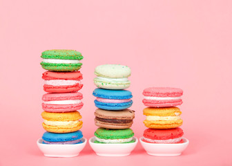 Macaron cookies in tiny white dishes stacked in graduated rows, colorful traditional french pastry on a pink background.