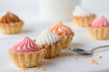 Small cakes and with cream on a white table with a spoon and a mug. Selective focus. 
