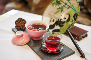 Red flower scented tea in pink porcelain bowl and glass cup with traditional panda pattern chinese fan