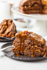 Piece of homemade snickers cake with chocolate cream and caramel on a black saucer, white background.