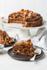 Piece of homemade snickers cake with chocolate cream and caramel on a black saucer, white background.