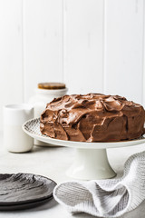 Homemade whole chocolate cake with chocolate cream and caramel on cake plate, white background.