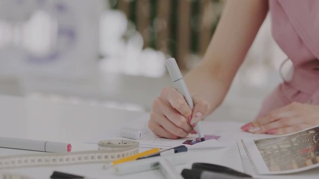 Female fashion designer with beautiful manicure drawing sketches. Dressmaker or couturer drawing cloth sketch by marker. Empty space for titles with blured background in frame.