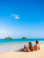 Beach vacation couple relaxing sunbathing on hawaiian tropical beach in Lanikai, Oahu, Hawaii, USA....