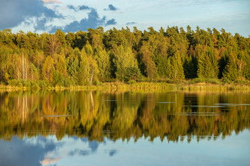 beautiful sunset by the lake with green grass meadow and white clouds in the blue sky