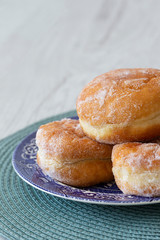 Jam doughnuts on a blue and white plate and green table mat on a grey wood background