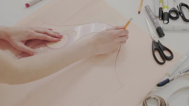Closeup of seamstress while she working with measure curve or pattern. Womans hands attentively and carefully circles the pattern with a pencil. Graph paper or plotting paper. Desktop of tailor.
