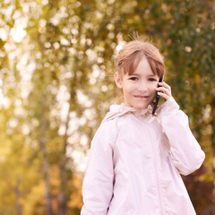 Young happy girl talks cellphone. Phone roaming. People with smartphone. Autumn background