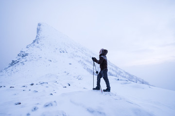 Naklejka na ściany i meble Man climber with trekking poles standing on snowy mountain peak