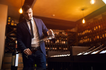 stylish young man in blue suit and white shirt pouring wine from decanter to the glass. close up...