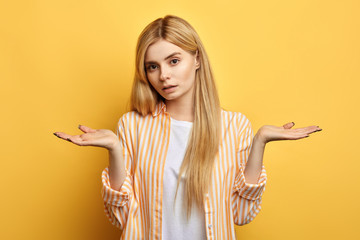 woman has displeased expression, wears striped shirt,white T-shirt, poses against yellow studio...