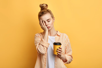 Tired sleepy woman holds a cup of coffee, has sad expression, closes eyes, cannot wake up in the morning and go to work. difficult, hard monday. isolated yellow background - 267732050