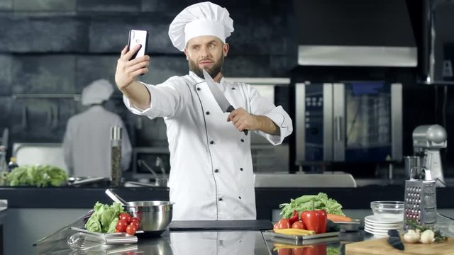 Chef making photo at kitchen. Chef with knife taking selfie at mobile phone.